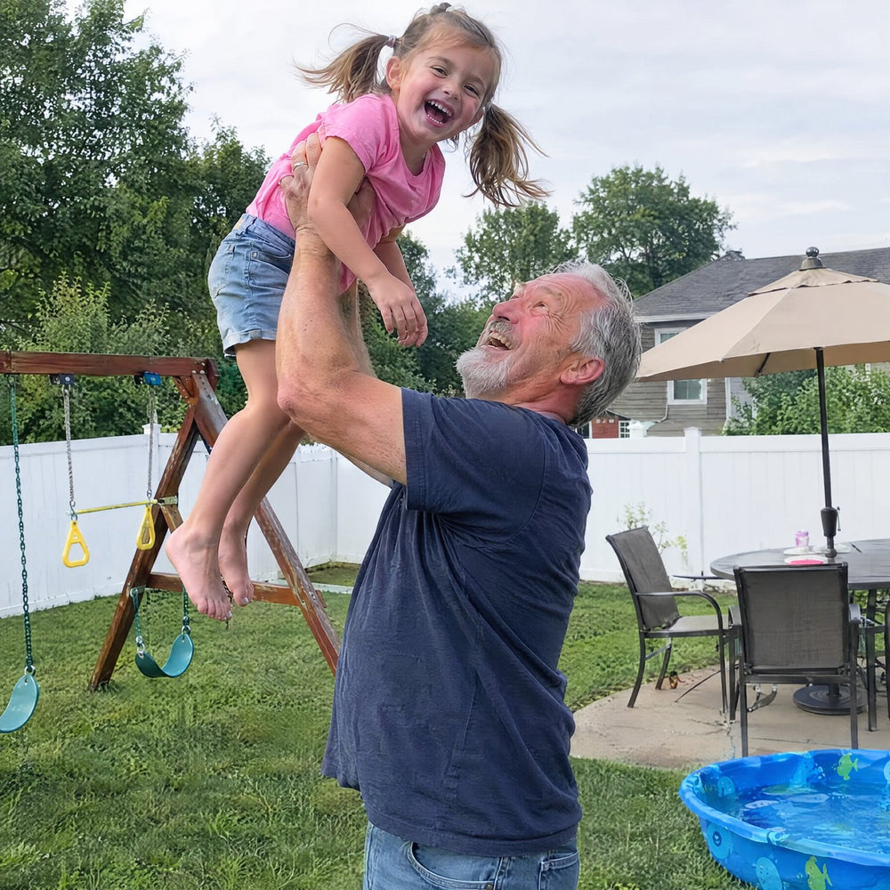 Grandfather lifting his granddaughter in the backyard