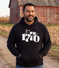 Man wearing The Answer To 1984 Is 1776 Hoodie in black on a farm road by a red barn