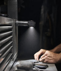 Headlamp stuck to a steel toolbox by its magnetic tailcap, lighting a workbench hands-free