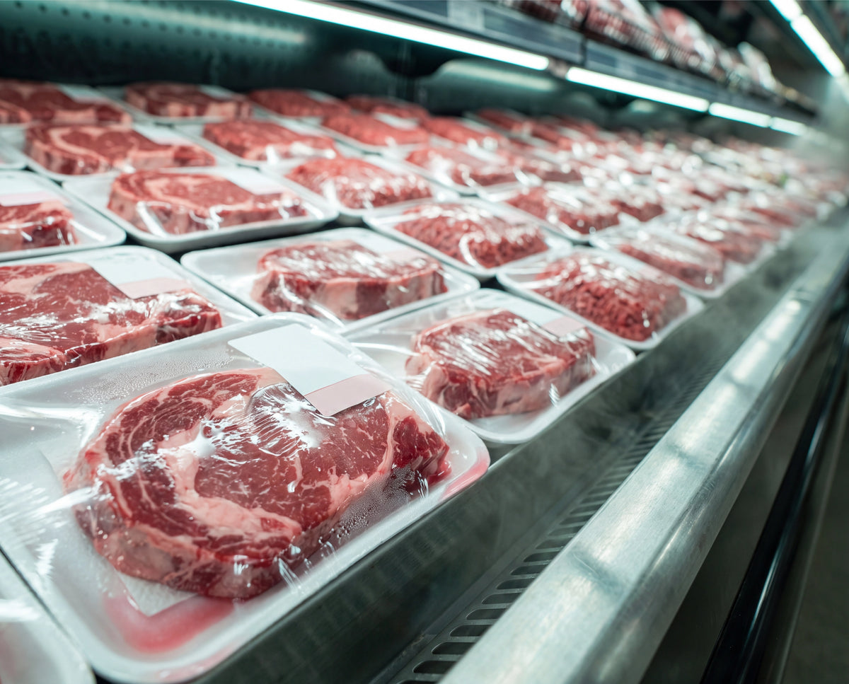 A grocery store meat case filled with steaks and ground beef sealed under plastic wrap
