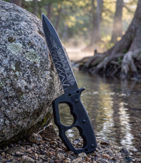 The Alex Jones Store - Molon Labe Trench War Dagger leaning against a granite boulder beside a Hill Country creek